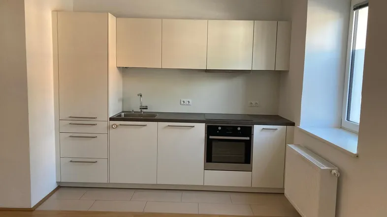 Moderne Einbauküche mit weißen Schränken, integrierten Geräten und einem Fenster für Tageslicht.