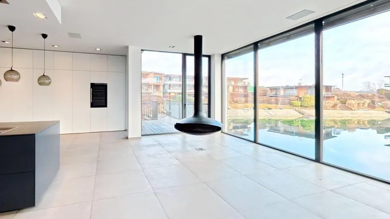 Geräumiges Wohnzimmer mit schwebendem Kamin, großen Fensterfronten und Blick auf den See.