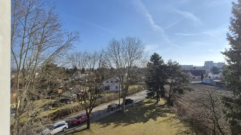 Blick vom Balkon auf die grüne Umgebung mit Bäumen und einer Straße unter blauem Himmel.