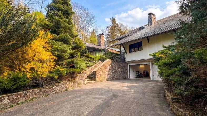 Einfahrt zum Haus mit integrierter Garage und umgebender Natur.