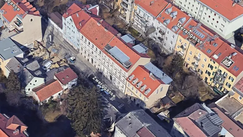 Luftaufnahme eines Wohngebäudes mit umliegenden Straßen und Dächern in städtischer Umgebung.