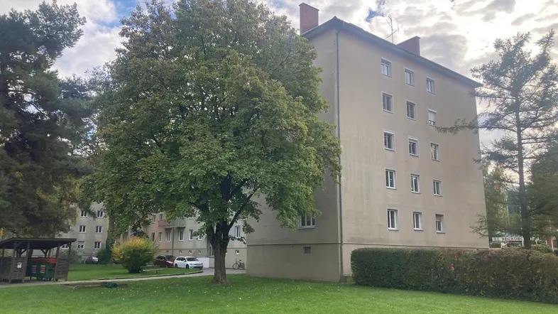 Mehrfamilienhaus mit beiger Fassade, umgeben von Bäumen und einer Grünfläche.