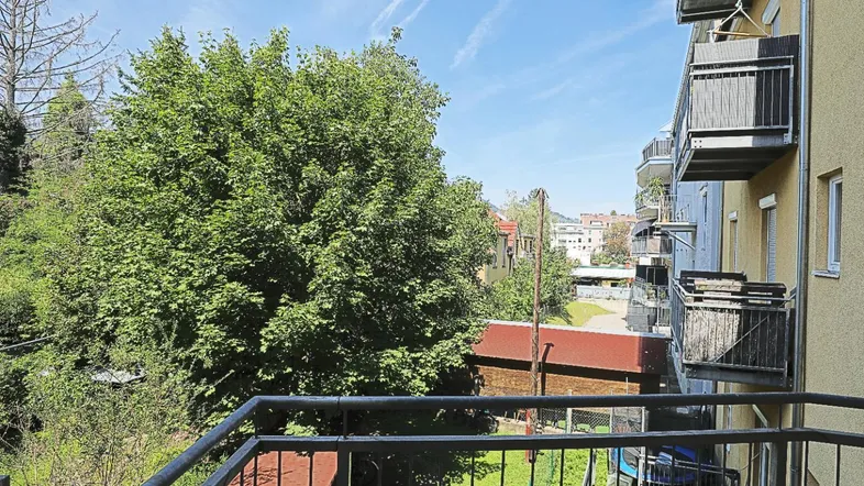 Balkon mit Blick ins Grüne und auf die umliegenden Gebäude unter blauem Himmel.