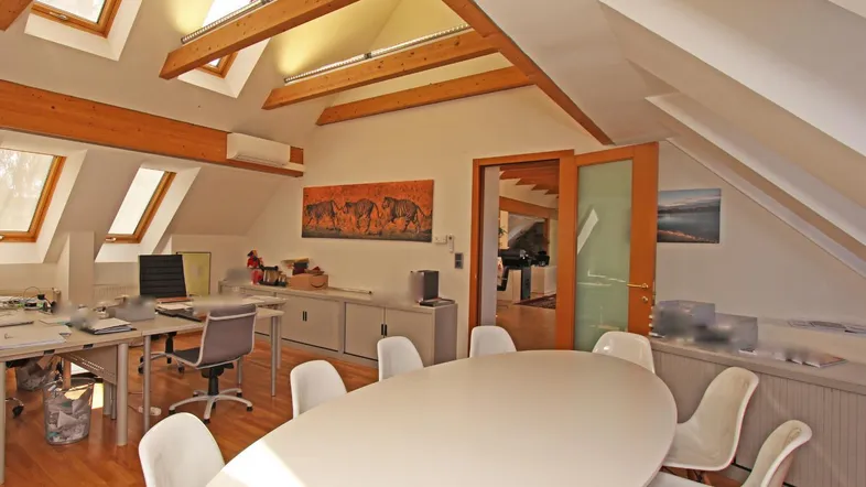 Geräumiges Dachgeschossbüro mit Holzbalken, vielen Dachfenstern und einem großen Konferenztisch.