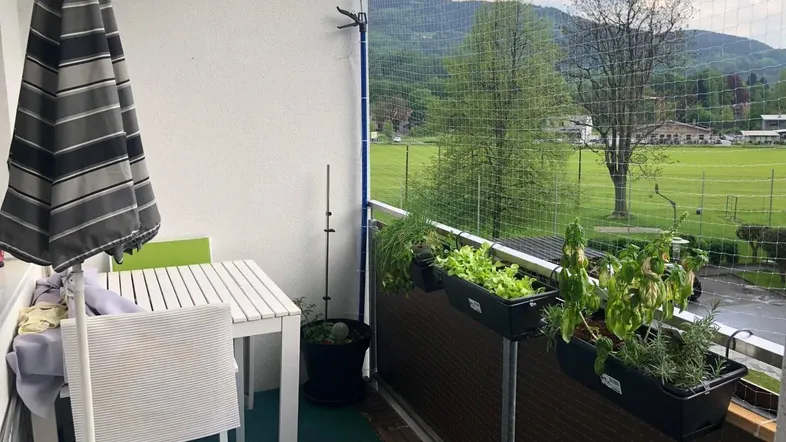 Möblierter Balkon mit Esstisch, Sonnenschirm und weitem Blick ins Grüne sowie auf die Berge.