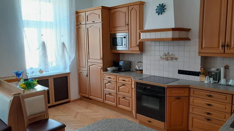 Helle Küche mit Holzschränken, Einbaugeräten und einem kleinen Essbereich mit Parkettboden.