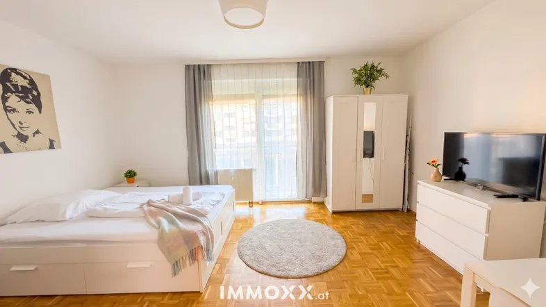 Helles Schlafzimmer mit Parkettboden, Balkonzugang und moderner Einrichtung.