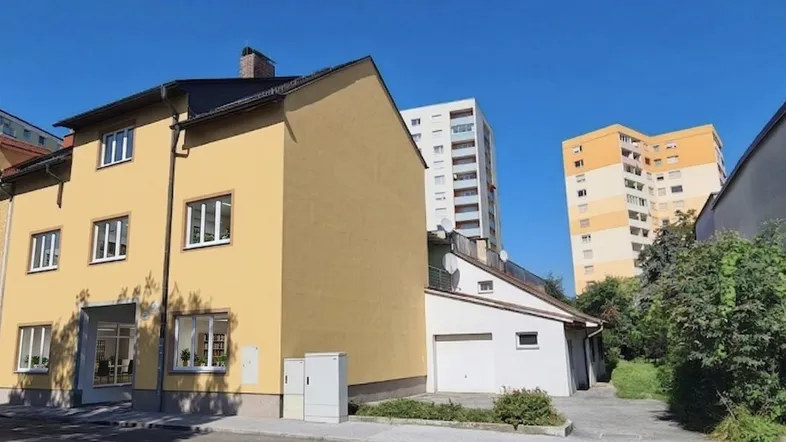 Gelbes Mehrfamilienhaus mit Garage und Blick auf höhere Gebäude im Hintergrund.