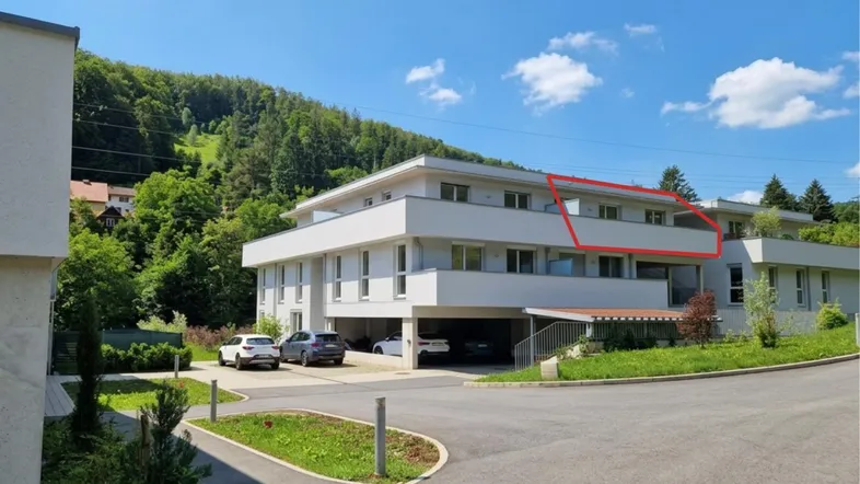 Modernes Apartmentgebäude mit mehreren Balkonen und Tiefgaragenzufahrt, umgeben von grüner Landschaft.