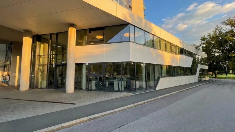 Modernes Bürogebäude mit großer Glasfassade und hellem Eingangsbereich bei Sonnenuntergang.
