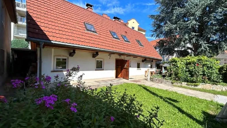 Charmantes Haus mit rotem Ziegeldach, Dachfenstern und gepflegtem Vorgarten unter blauem Himmel.