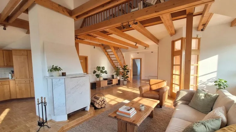 Helles Wohnzimmer mit Holzbalken, Kamin und offener Galerie, die einen gemütlichen Wohnbereich schafft.