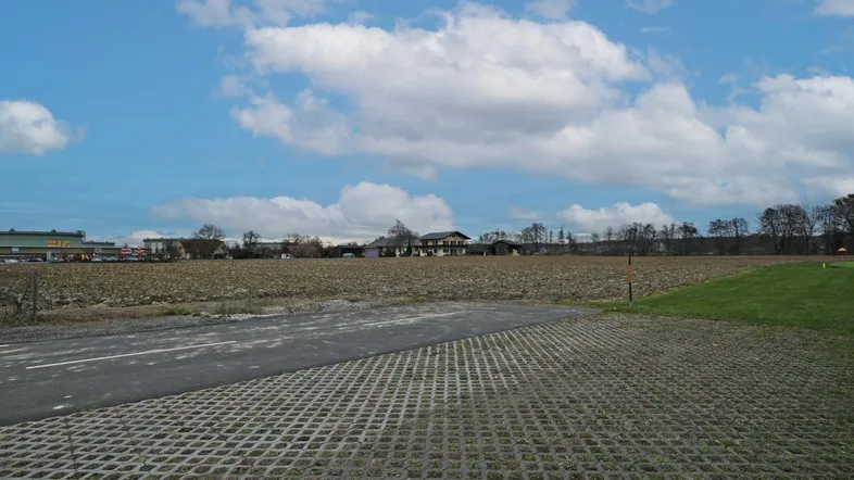 Weitläufiges Grundstück mit Ackerfläche und einem gepflasterten Bereich unter blauem Himmel.