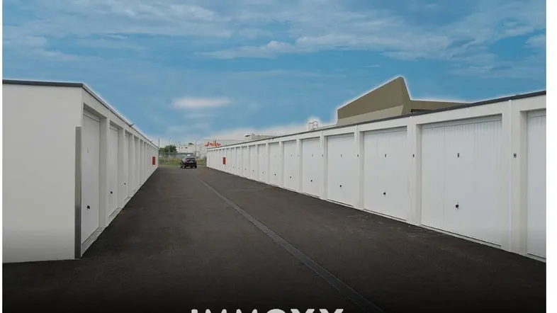 Lange Reihe weißer Garagenboxen entlang einer asphaltierten Zufahrt unter blauem Himmel.