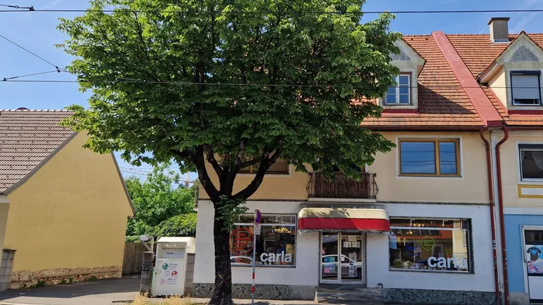 Mehrstöckiges Gebäude mit Geschäftsfassade im Erdgeschoss und Wohnungen darüber, an einer belebten Straße gelegen.
