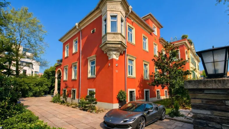 Prächtige Villa mit roter Fassade, Erker und gepflasterter Auffahrt unter blauem Himmel.