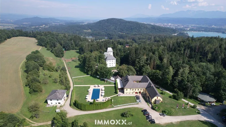 Luftaufnahme eines weitläufigen Anwesens mit mehreren Gebäuden, Pool und umgebender Naturlandschaft.