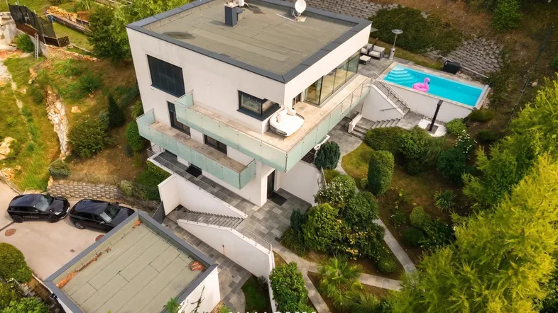 Moderne Villa mit Flachdach, Swimmingpool und weitläufigem Garten in grüner Umgebung.