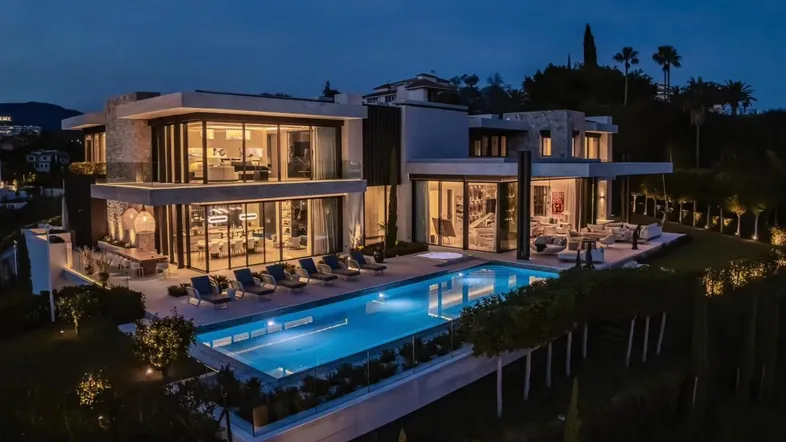 Luxuriöse moderne Villa bei Nacht mit beleuchtetem Pool und großzügigen Terrassenbereichen.