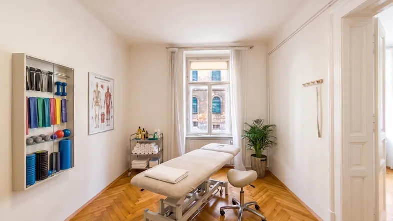 Heller Raum mit Fischgrätparkett, Therapieliege und Sportgeräten, ideal für Praxisräume.