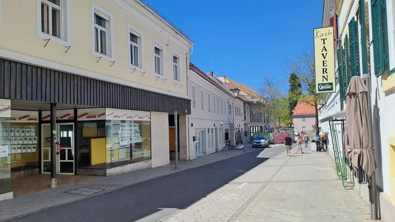 Eine belebte Straße mit Geschäften und einem Gasthaus unter strahlend blauem Himmel.