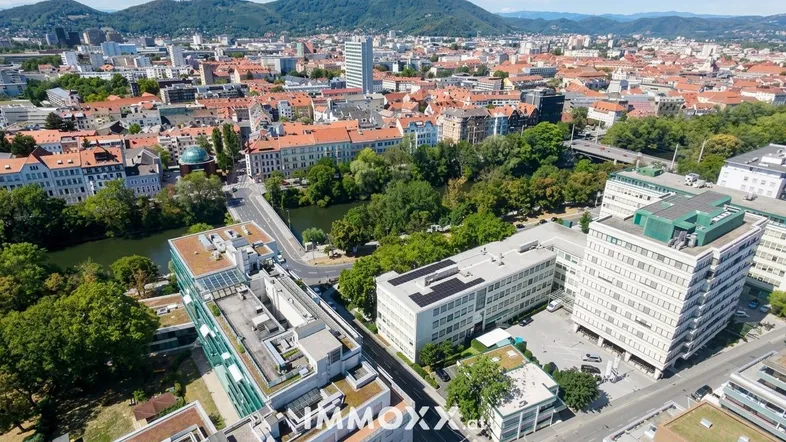 Panoramablick auf die Stadt mit Fluss, Gebäuden und grünen Hügeln im Hintergrund.