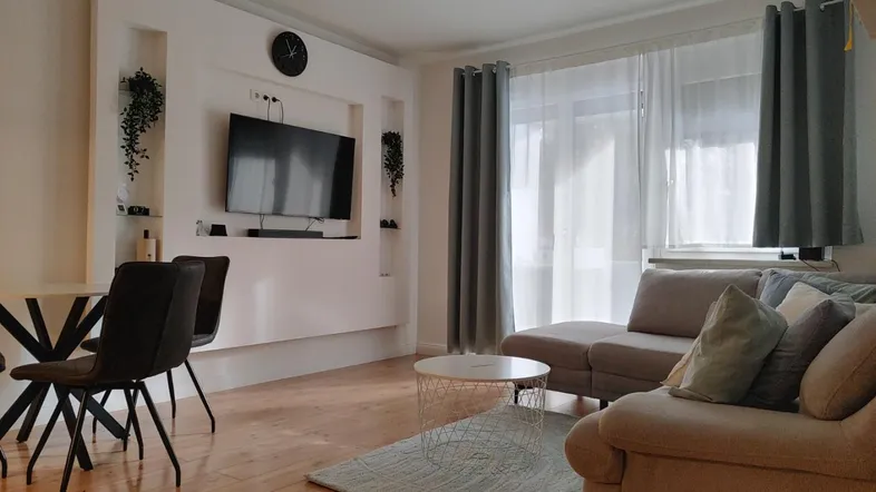 Heller Wohn- und Essbereich mit modernem TV-Möbel, bequemer Couch und Holzboden.