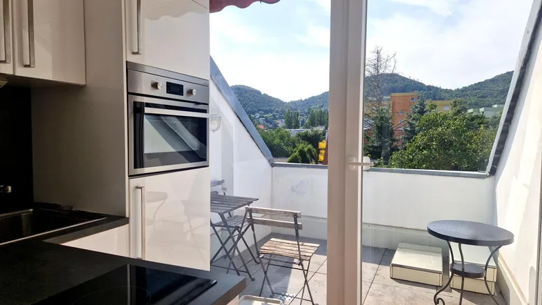 Moderne Küche mit weißen Schränken, integriertem Backofen und direktem Zugang zu einer sonnigen Dachterrasse mit Bergblick.