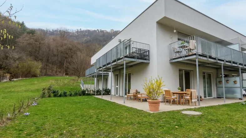 Modernes Gebäude mit großer Rasenfläche, möblierter Terrasse und Balkonen mit Blick ins Grüne.