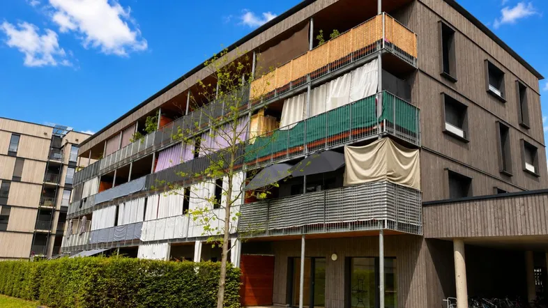 Modernes Mehrfamilienhaus mit Holzfassade, Balkonen und gepflegter Grünfläche.