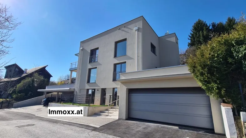 Modernes Gebäude mit klarer Architektur, integrierter Garage und Carport unter blauem Himmel.