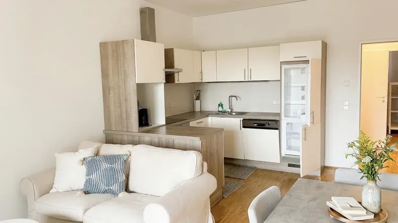 Offener Wohn-Essbereich mit integrierter Küche, hellem Sofa und modernem Esstisch.
