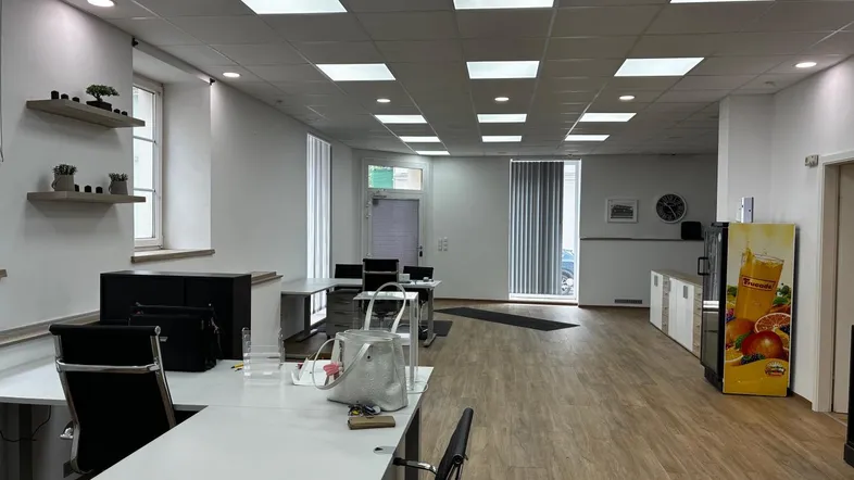 Geräumiges und helles Büro mit mehreren Arbeitsplätzen, Holzfußboden und modernen Deckenleuchten.
