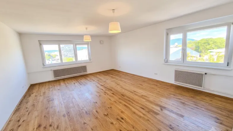 Helles, leeres Zimmer mit Holzboden und großen Fenstern, die einen weiten Blick bieten.