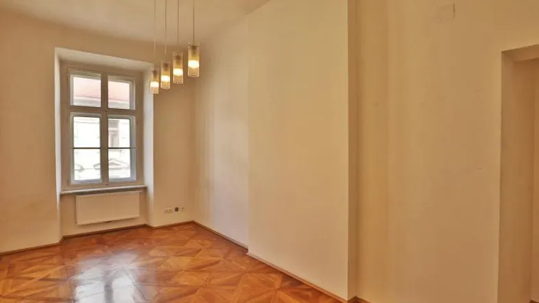 Helles Zimmer mit Fischgrätparkettboden und einem Fenster, das Tageslicht hereinlässt.