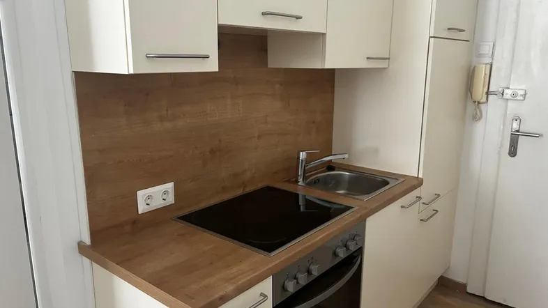 Kleine, funktionale Küche mit hellen Schränken, Holzoptik-Arbeitsplatte und integriertem Herd.