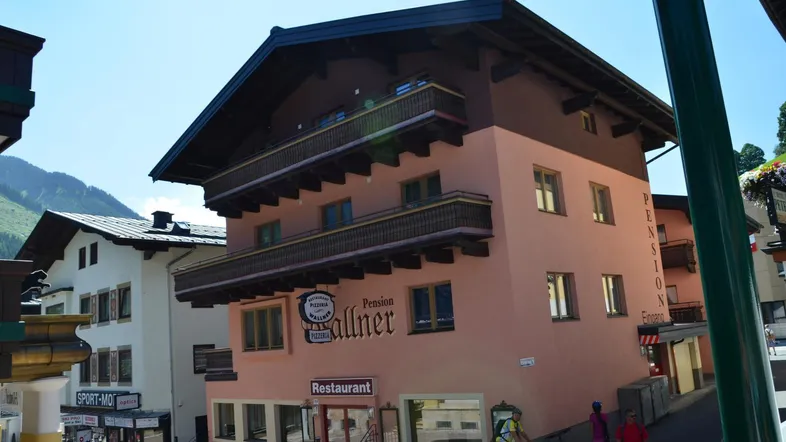 Traditionelles Gebäude mit alpiner Architektur, Balkonen und einem Restaurant im Erdgeschoss.