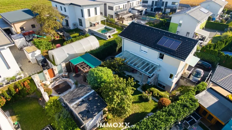 Luftaufnahme eines Wohngebiets mit mehreren Häusern, Gärten und Solaranlagen auf den Dächern.