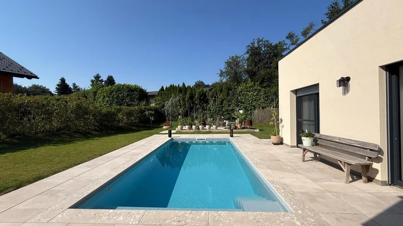 Moderner Außenpool mit gefliester Terrasse und Liegewiese unter blauem Himmel.