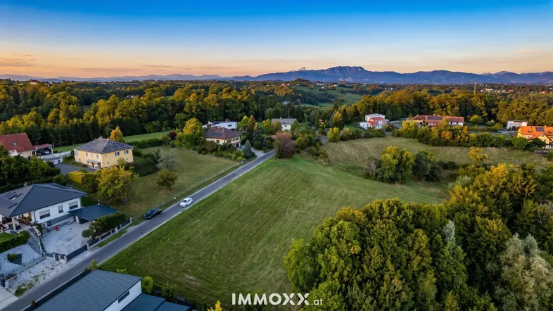 Panoramablick über die ländliche Umgebung mit Häusern, Feldern und Bergen im Hintergrund bei Sonnenuntergang.