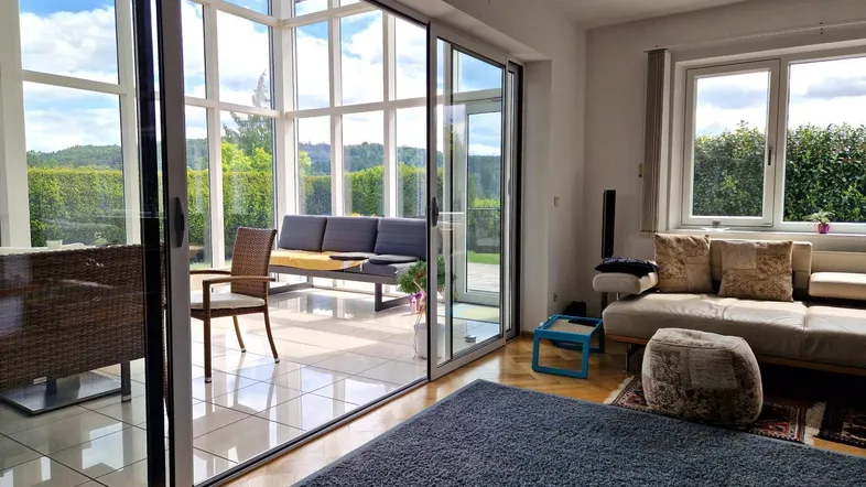 Helles Wohnzimmer mit großen Glasschiebetüren, die zu einem Wintergarten mit Blick ins Grüne führen.