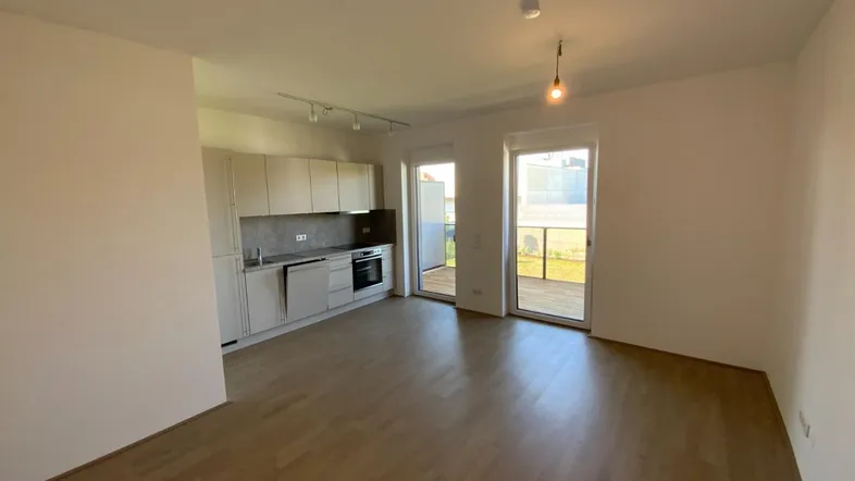 Heller offener Wohn-Essbereich mit integrierter Küchenzeile und Zugang zum Balkon.