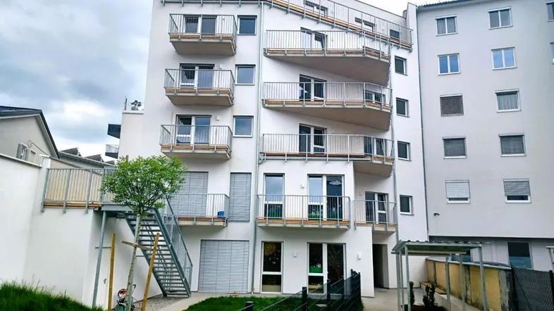 Moderne Wohnanlage mit mehreren Balkonen und Zugang zu einer Grünfläche im Außenbereich.