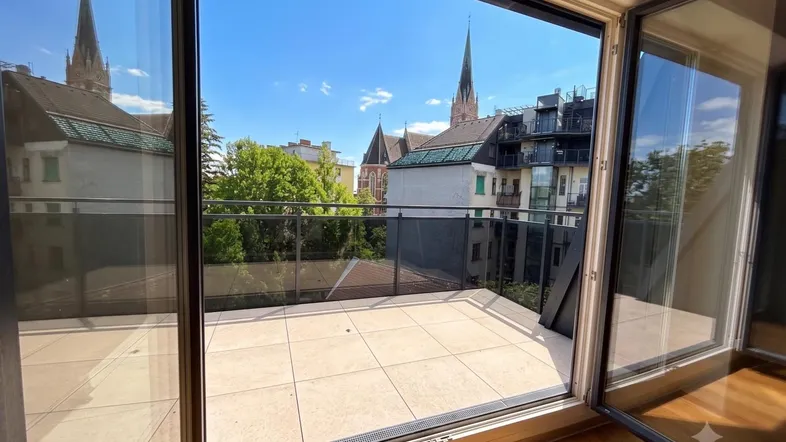 Blick von einer modernen Terrasse mit Fliesenboden auf eine Stadtlandschaft mit Kirchtürmen unter blauem Himmel.