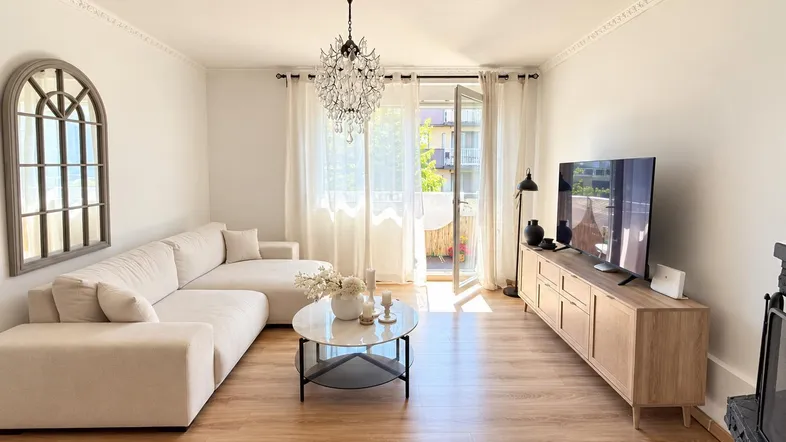 Helles Wohnzimmer mit modernem Sofa, Holzboden und Zugang zum Balkon.