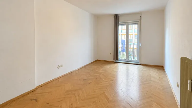 Heller Raum mit Fischgrätparkettboden und Zugang zu einem französischen Balkon.