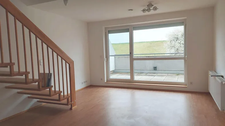 Helles Wohnzimmer mit Holztreppe, Laminatboden und Zugang zu einer Terrasse mit Blick ins Grüne.