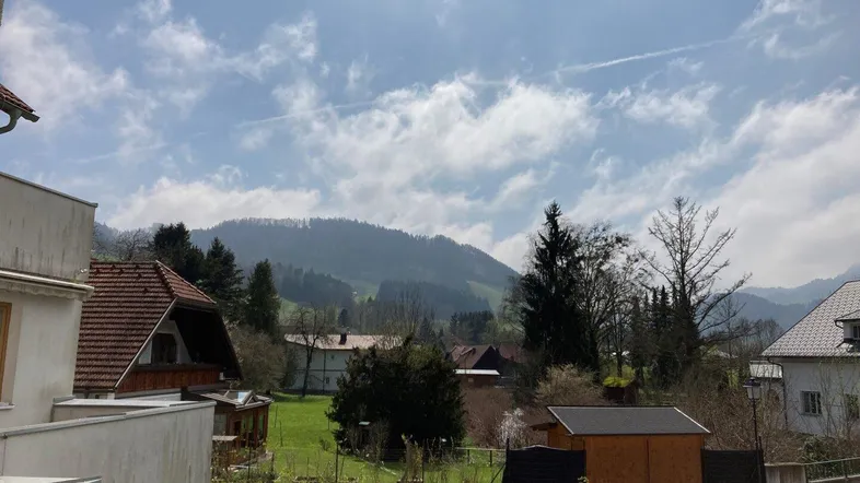 Ländliche Aussicht auf bewaldete Hügel und umliegende Häuser unter blauem Himmel.
