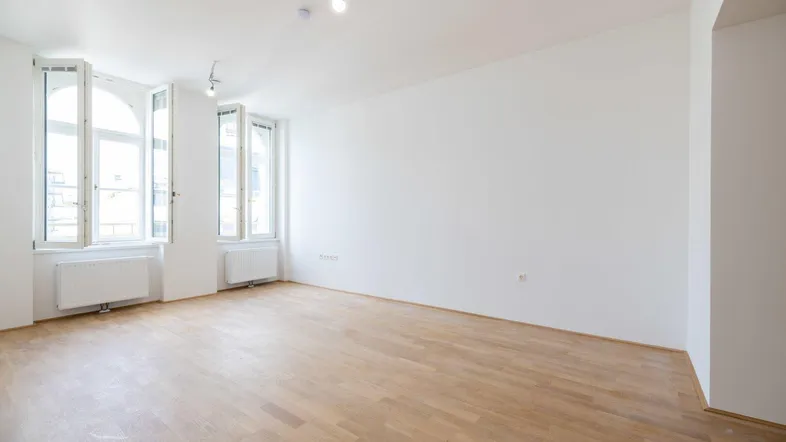 Helles, leeres Zimmer mit Parkettboden und hohen Fenstern, bereit zur individuellen Gestaltung.