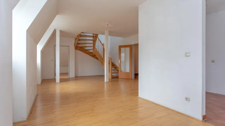 Heller, leerer Wohnbereich mit Holztreppe und Parkettboden, bereit zur individuellen Gestaltung.